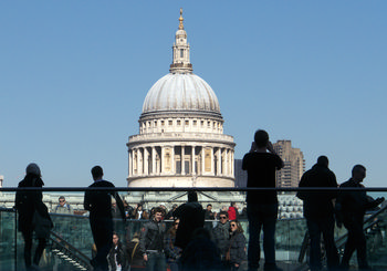 Millenium bridge St Pauls This urban architecture photograph was taken late in the morning during spring. The image prominently displays the Millennium Bridge in London, United Kingdom, with many people crossing the structure. St Paul's Cathedral, a well-known church and architectural landmark, is clearly visible in the background, its iconic dome dominating the skyline. The photograph captures the dynamic city atmosphere of London, showcasing both the bridge and the cathedral as significant elements of the city's architectural heritage. The scene emphasizes the connection between the modern Millennium Bridge and the historic St Paul's Cathedral, illustrating the blend of old and new found in this area of London.